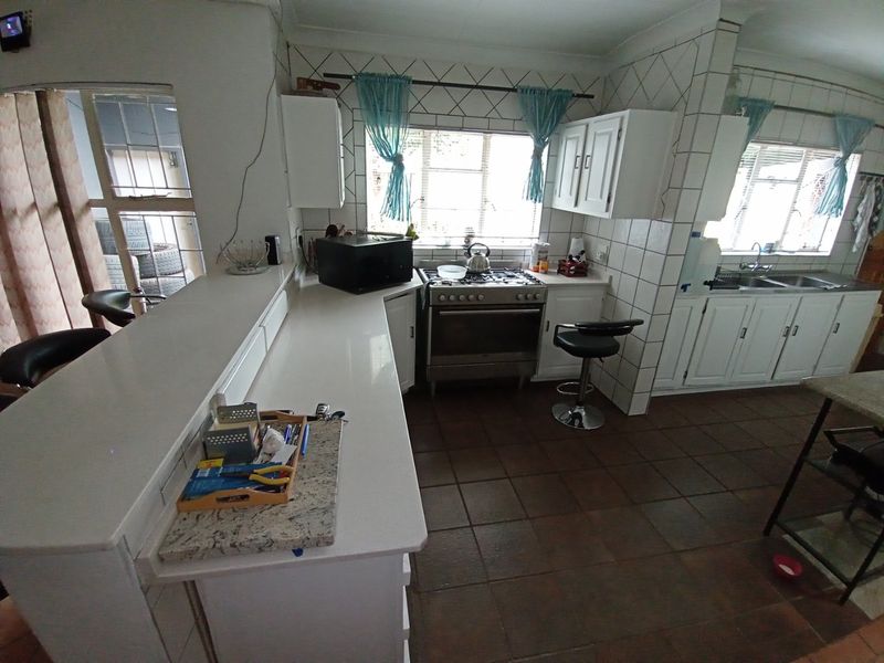 A functional kitchen featuring white cabinetry, a gas stove, tiled backsplash, and a breakfast bar, with tiled flooring throughout.