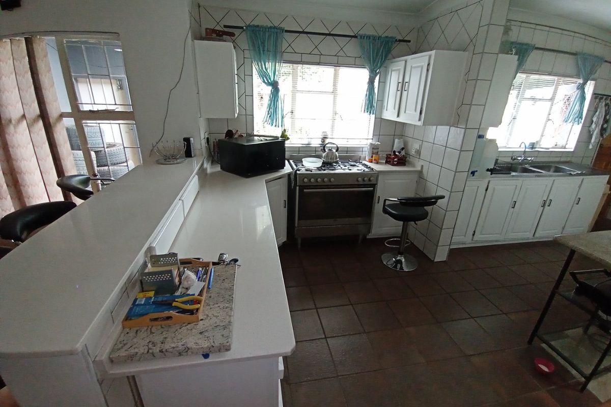A functional kitchen featuring white cabinetry, a gas stove, tiled backsplash, and a breakfast bar, with tiled flooring throughout.
