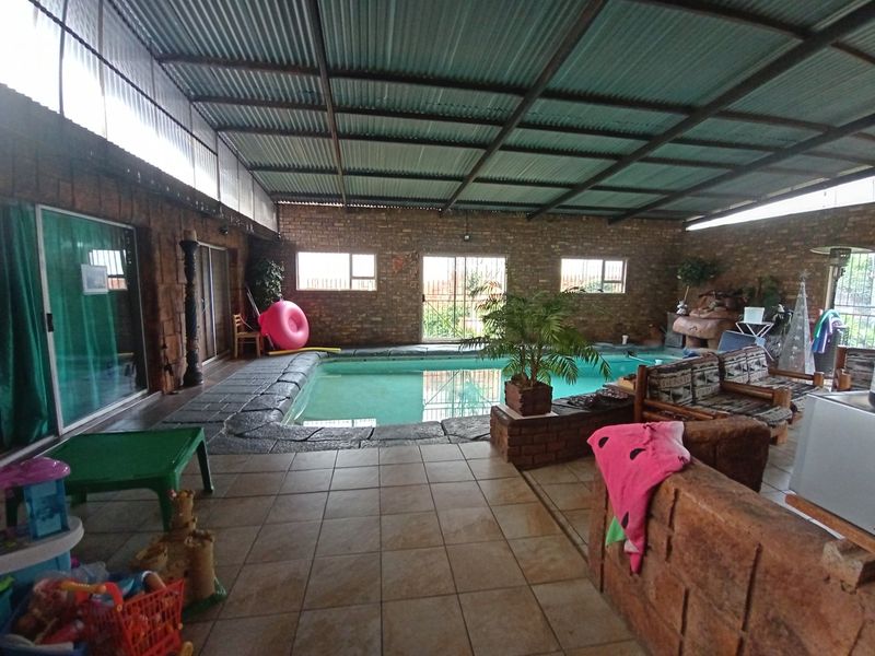 An enclosed indoor swimming pool area featuring exposed brick walls, tiled flooring, and a corrugated metal roof, providing a versatile year-round entertainment space.