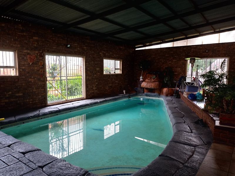 Indoor swimming pool area featuring exposed brick walls, a corrugated metal roof, and stone coping, providing a sheltered space for year-round swimming.