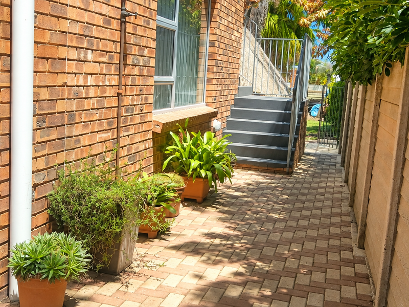 A side exterior view of the property featuring a brick facade, paved walkway, and an external staircase leading to an upper level.