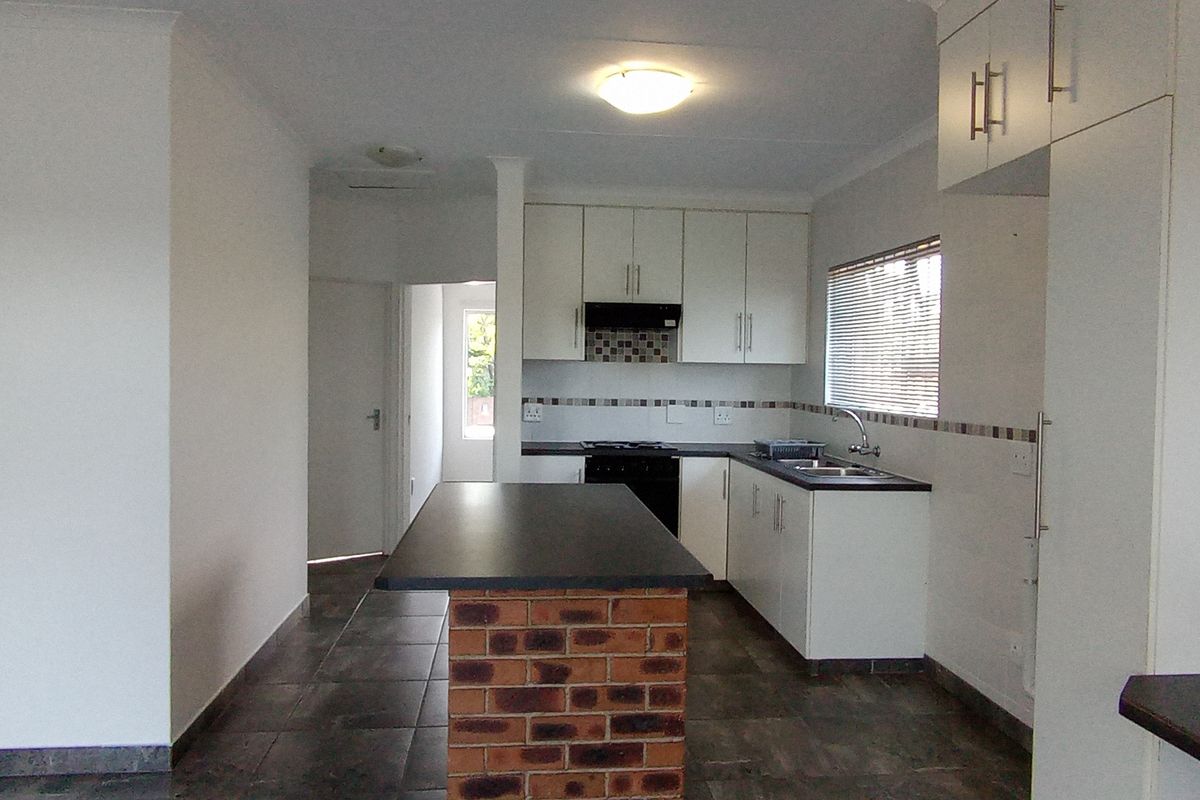 A clean, functional kitchen featuring white cabinetry, dark laminate countertops, a unique brick-base island, and tiled flooring in an open-plan layout.