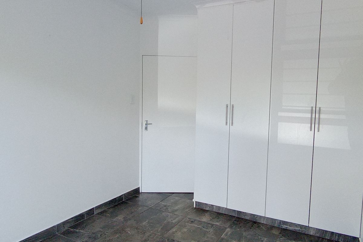 A clean, empty bedroom featuring modern white built-in cupboards and dark tiled flooring.