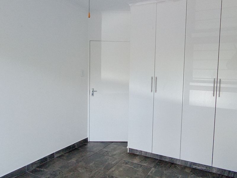 A clean, empty bedroom featuring modern white built-in cupboards and dark tiled flooring.