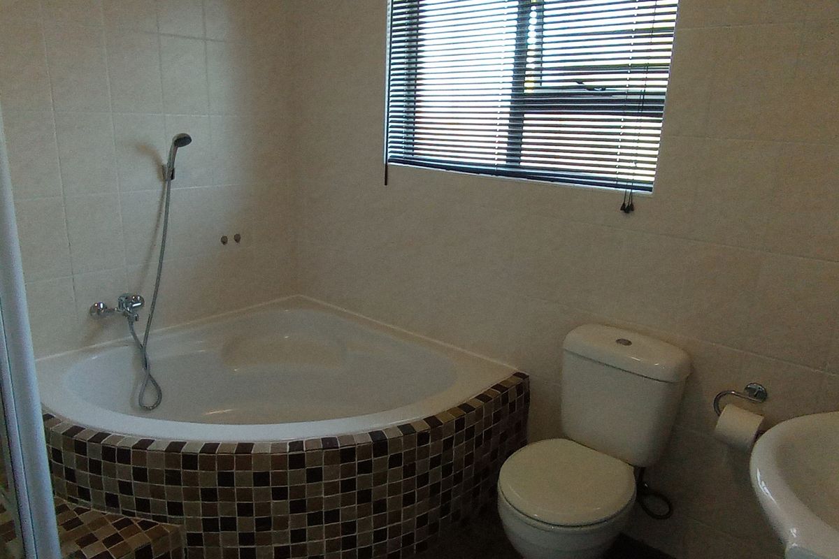 A functional bathroom featuring a corner bathtub with mosaic tiling, a separate shower enclosure, a pedestal basin, and a toilet.