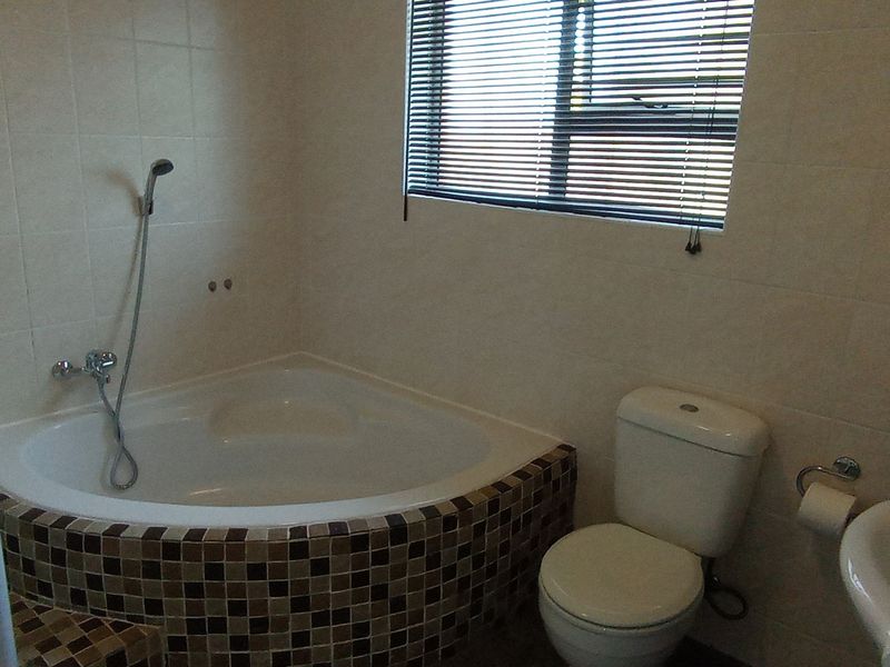 A functional bathroom featuring a corner bathtub with mosaic tiling, a separate shower enclosure, a pedestal basin, and a toilet.