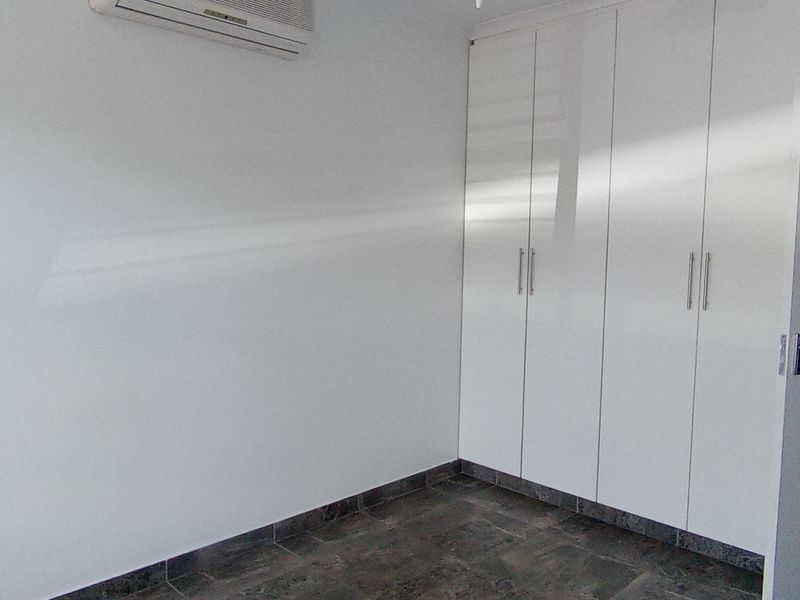 A clean, empty bedroom featuring white built-in cupboards, tiled flooring, and a wall-mounted air conditioning unit.