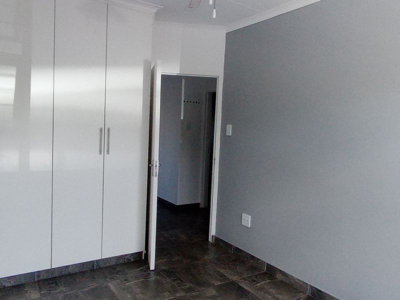 A clean, empty bedroom featuring modern white built-in cupboards, grey painted walls, and dark tiled flooring.