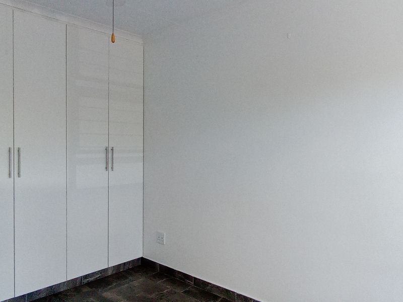 A clean, empty bedroom featuring modern white built-in cupboards and dark tiled flooring, providing a neutral canvas for personalization.