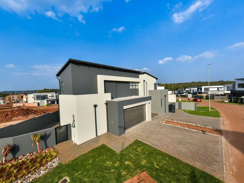 Modern double-story residential property featuring a paved driveway, double garage, and landscaped front garden in a contemporary estate setting.