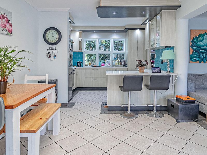 An open-plan living and kitchen area featuring tiled flooring, a central kitchen island with breakfast bar seating, and modern cabinetry with a blue tiled backsplash.