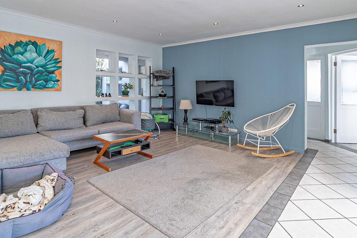 A bright living room featuring laminate flooring, recessed downlighting, and a feature blue wall, with an adjacent tiled entryway.