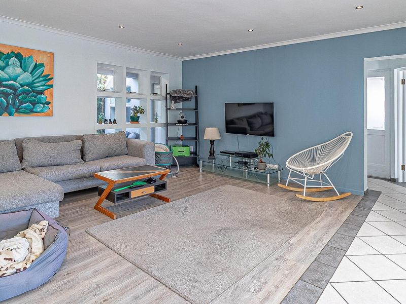 A bright living room featuring laminate flooring, recessed downlighting, and a feature blue wall, with an adjacent tiled entryway.