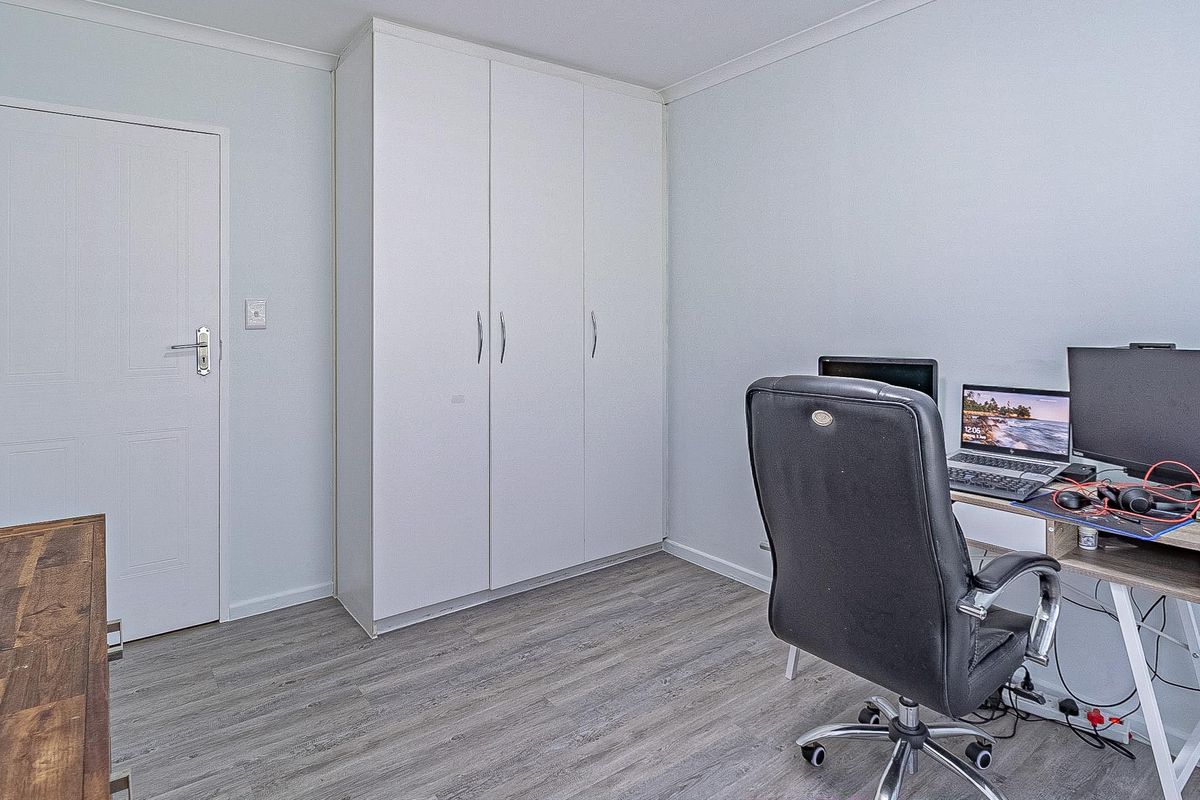 A clean bedroom featuring light-toned laminate flooring and a white built-in wardrobe, offering a neutral and functional space.
