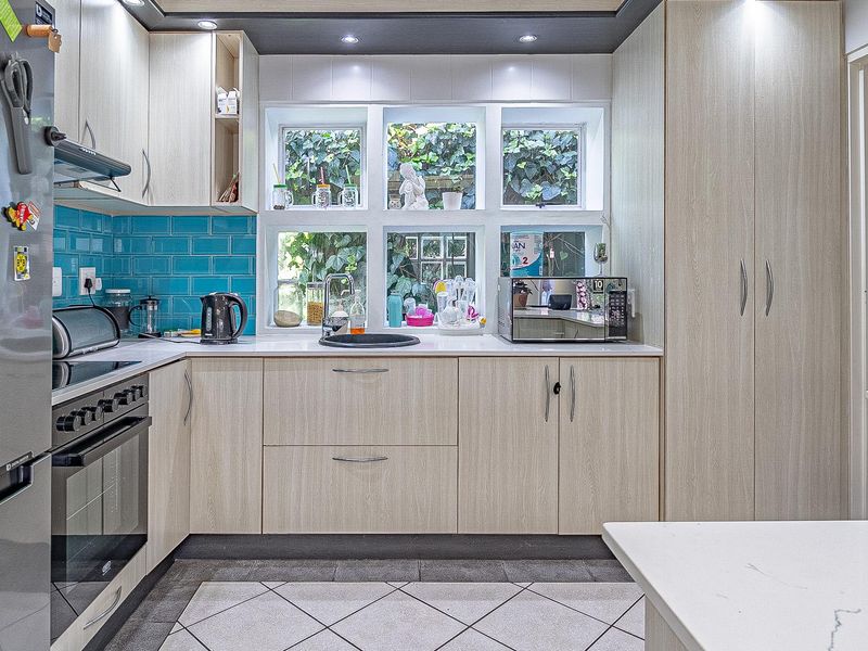 Modern kitchen featuring light wood cabinetry, vibrant blue subway tile backsplash, stone countertops, and integrated appliances with a view of the garden.