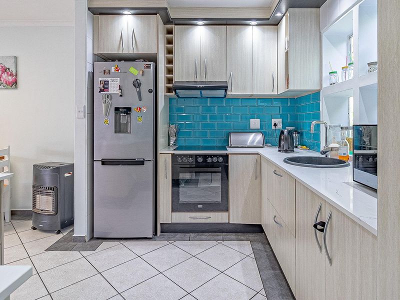 Modern kitchen featuring light wood cabinetry, vibrant blue subway tile backsplash, stone countertops, and integrated appliances, offering a functional and stylish cooking space.