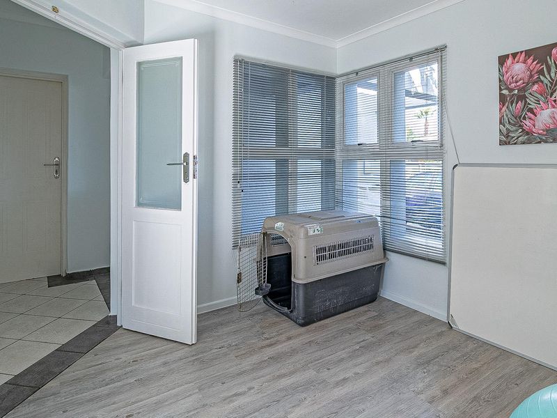 A bright, neutral office space featuring modern laminate flooring, venetian blinds, and a frosted glass panel door leading to the hallway.