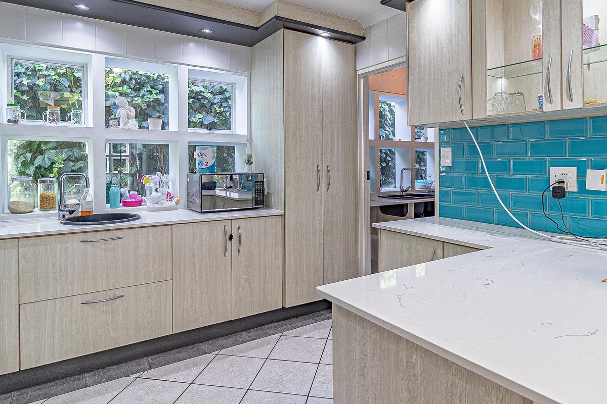 Modern kitchen featuring light wood cabinetry, vibrant blue subway tile backsplash, quartz countertops, and ample natural light through large windows.