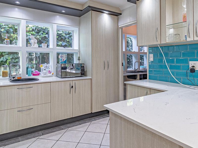 Modern kitchen featuring light wood cabinetry, vibrant blue subway tile backsplash, quartz countertops, and ample natural light through large windows.