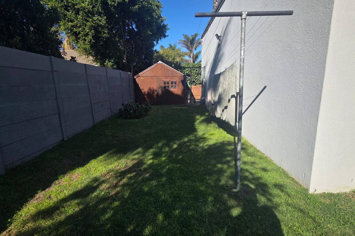 A rear garden area featuring a lawn, a wooden storage shed, and a precast concrete boundary wall.