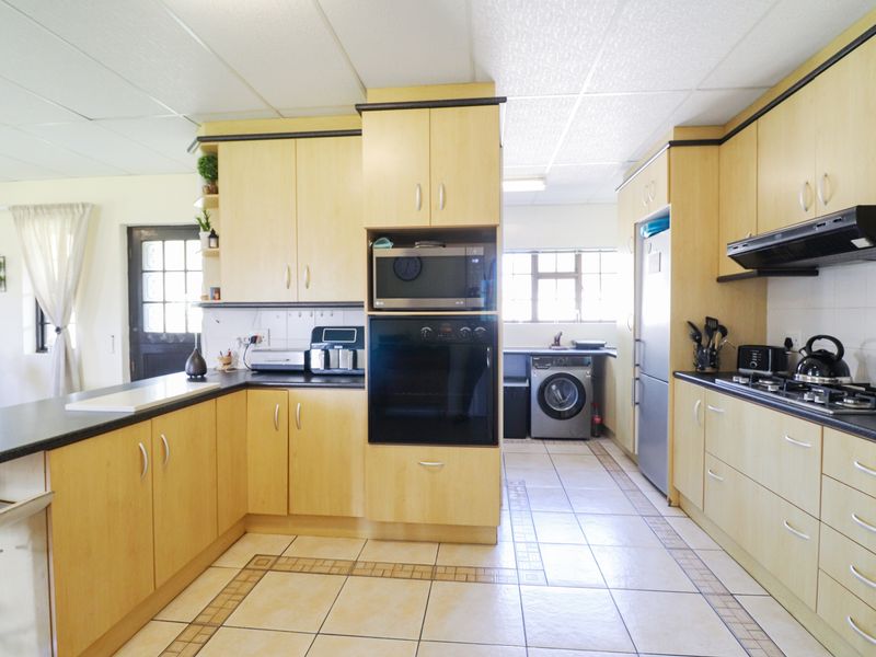 A functional kitchen featuring light wood-finish cabinetry, dark countertops, built-in oven and microwave, gas hob with extractor, and tiled flooring throughout.