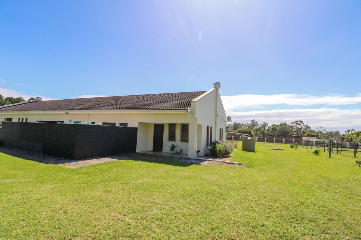 Rear view of the property featuring a covered patio, a spacious lawn, and a water tank, enclosed by a boundary fence.
