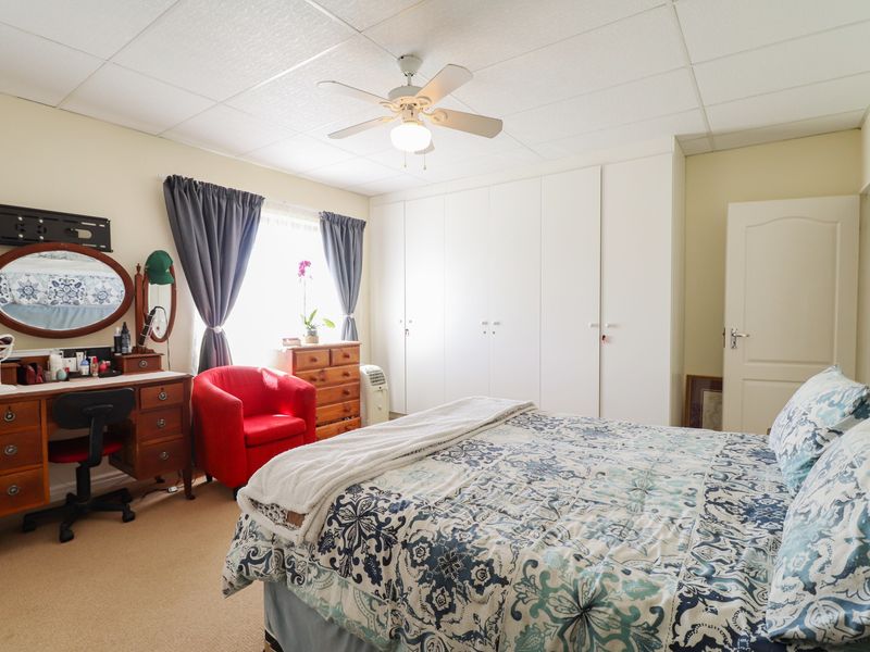 A well-lit bedroom featuring built-in floor-to-ceiling cupboards, a central ceiling fan, and neutral carpeting.