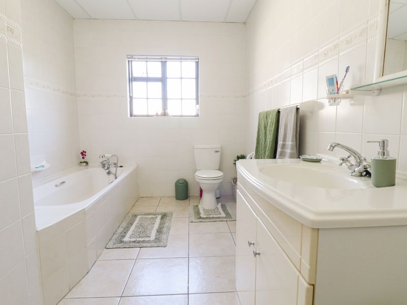 A functional bathroom featuring a built-in bathtub, a vanity cabinet with a washbasin, and a toilet, finished with neutral wall and floor tiles.