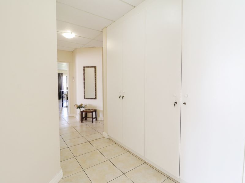 A bright hallway featuring extensive built-in storage cupboards and neutral tiled flooring, leading towards an open living area.