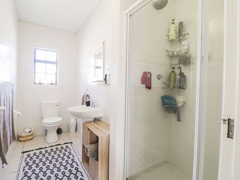 A functional bathroom featuring a shower enclosure, pedestal basin, and toilet with neutral wall and floor tiling.