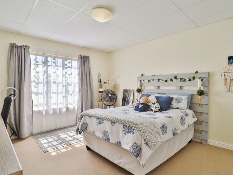 A well-lit bedroom featuring neutral wall tones, carpeted flooring, and a drop ceiling, offering a comfortable and functional living space.