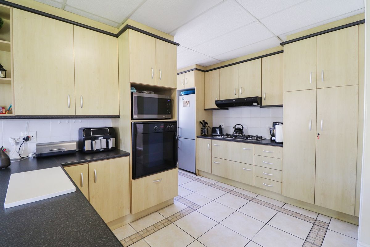 Functional kitchen featuring light wood-look cabinetry, dark countertops, built-in oven, gas hob, and tiled flooring throughout.