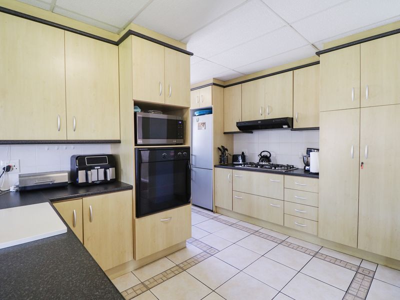 Functional kitchen featuring light wood-look cabinetry, dark countertops, built-in oven, gas hob, and tiled flooring throughout.