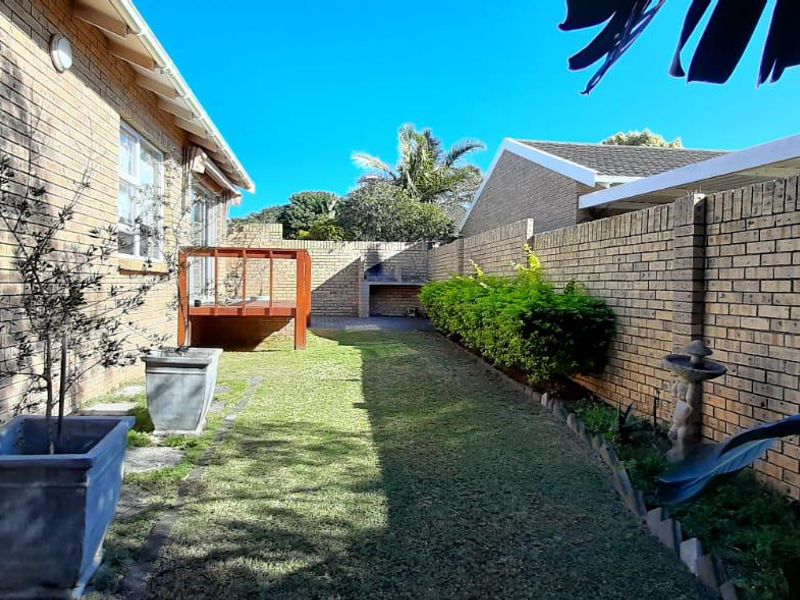A private rear garden featuring a brick boundary wall, a raised timber deck, and a built-in outdoor braai area.