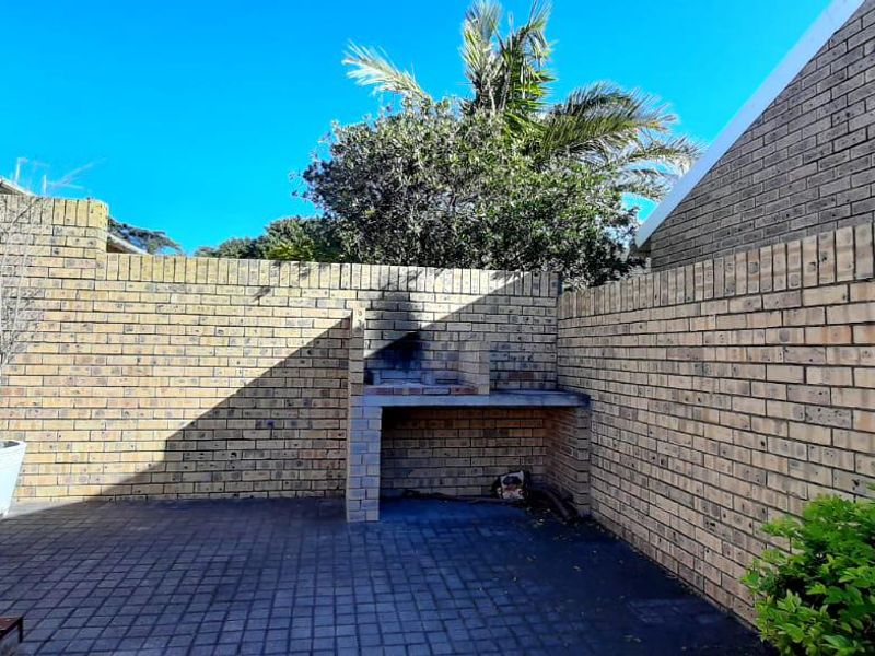 A private rear courtyard featuring a paved patio area and a built-in brick braai, enclosed by high brick boundary walls.