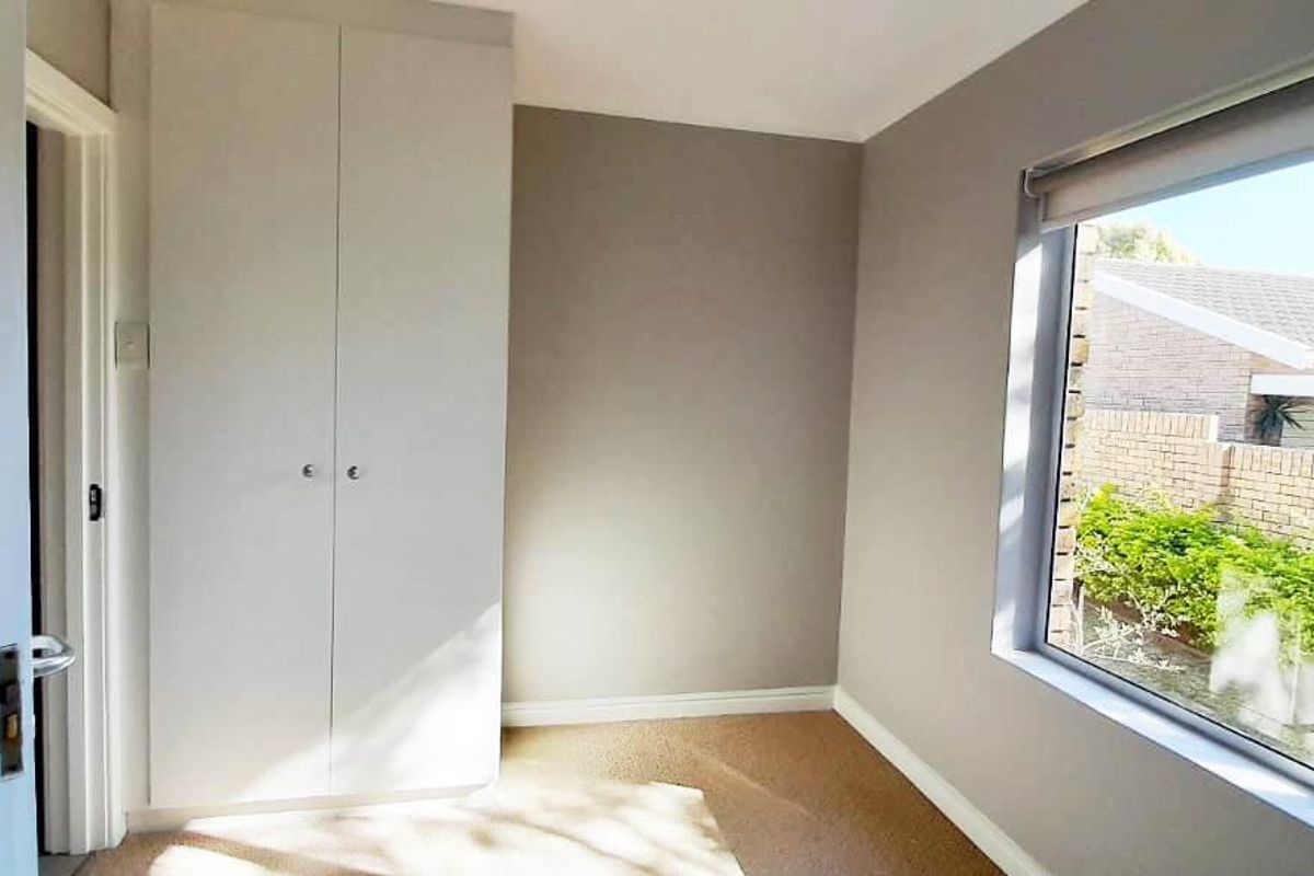 A bright, empty bedroom featuring neutral wall tones, a built-in wardrobe, and a large window with security bars overlooking the exterior.