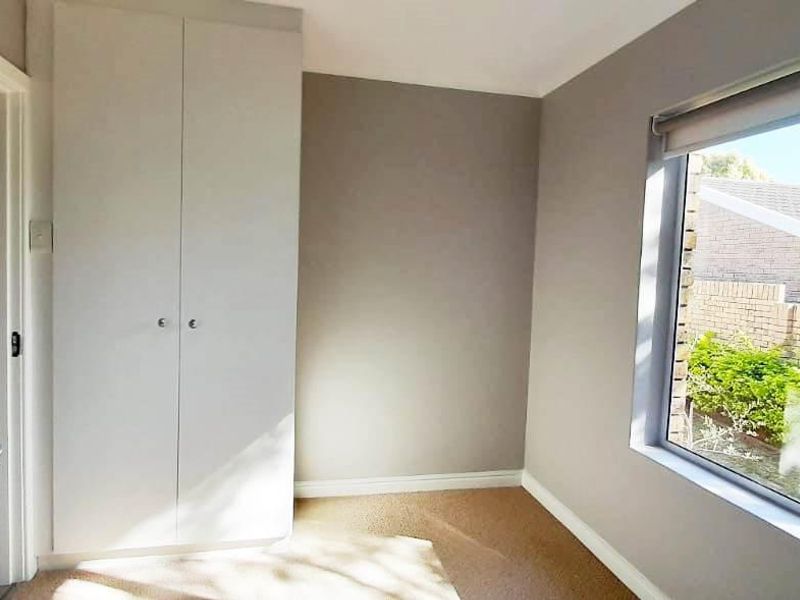 A bright, empty bedroom featuring neutral wall tones, a built-in wardrobe, and a large window with security bars overlooking the exterior.