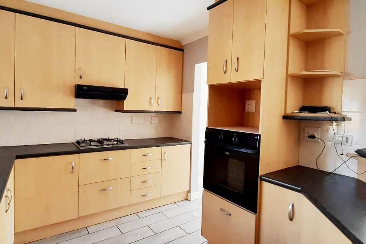 A functional kitchen featuring light wood-finish cabinetry, dark laminate countertops, a gas hob, extractor fan, and built-in oven with tiled flooring.