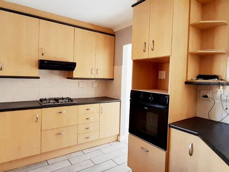 A functional kitchen featuring light wood-finish cabinetry, dark laminate countertops, a gas hob, extractor fan, and built-in oven with tiled flooring.