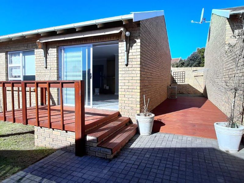 Rear exterior view of the townhouse featuring a timber deck, paved patio area, and sliding glass door access to the interior.