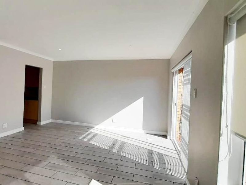 A bright and spacious open-plan living area featuring neutral walls, modern tiled flooring, and large sliding doors that provide ample natural light.