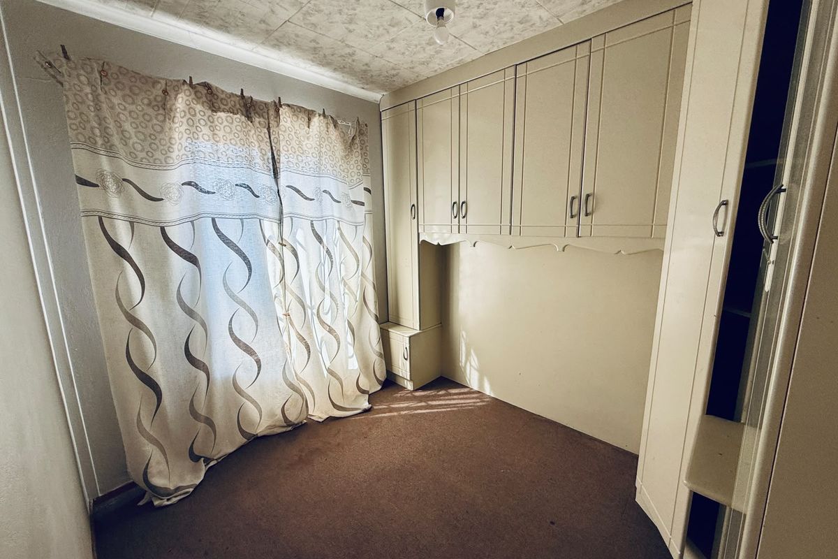 A bedroom featuring built-in cupboards, carpeted flooring, and patterned ceiling tiles, offering a functional space ready for modernization.