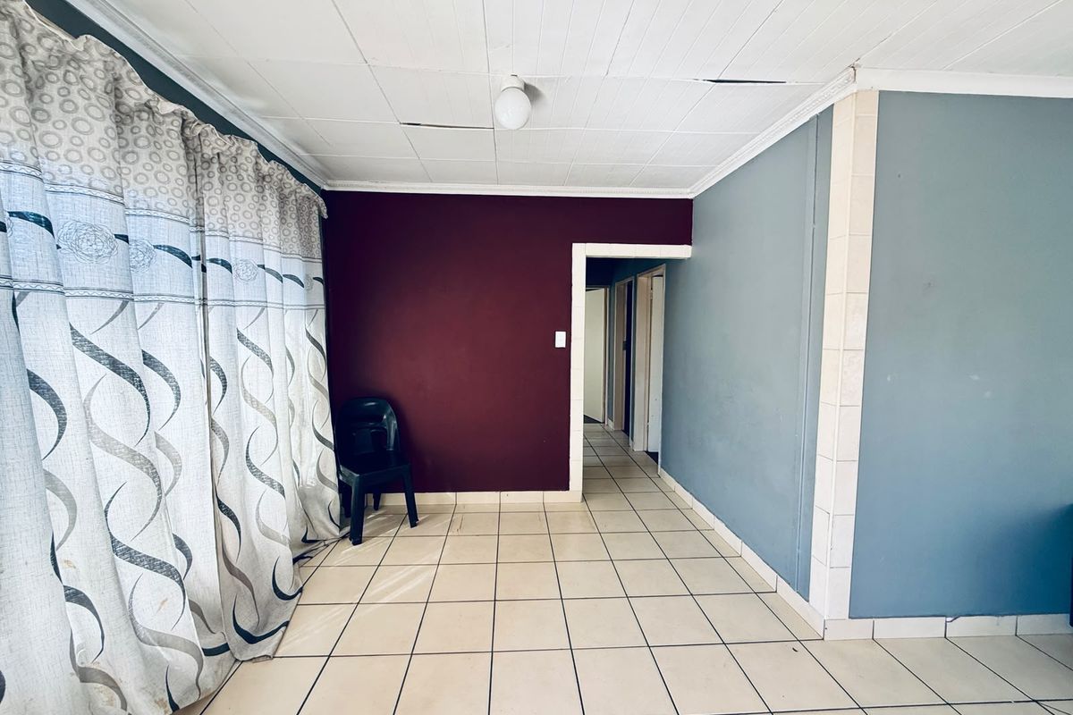 An empty living area featuring tiled flooring and a ceiling with visible damage, offering a blank canvas for renovation and interior design updates.