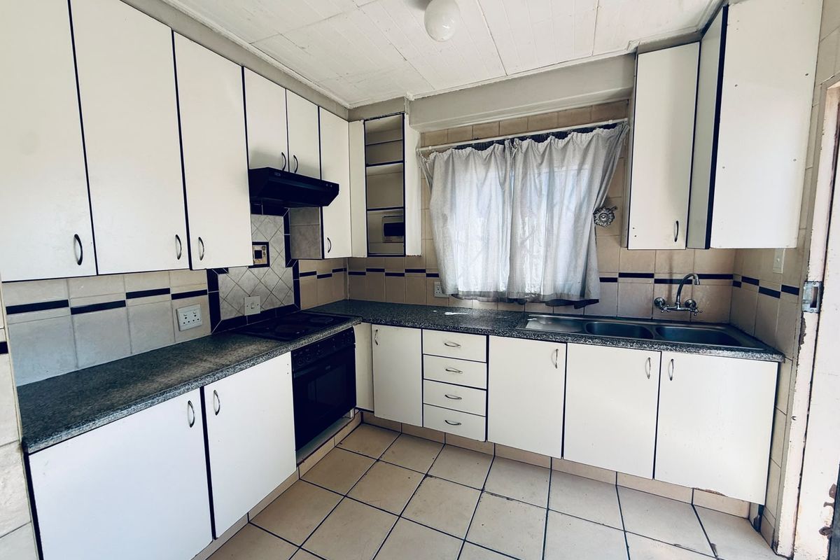 A dated kitchen featuring white built-in cabinetry, laminate countertops, a built-in oven with extractor fan, and tiled flooring throughout.