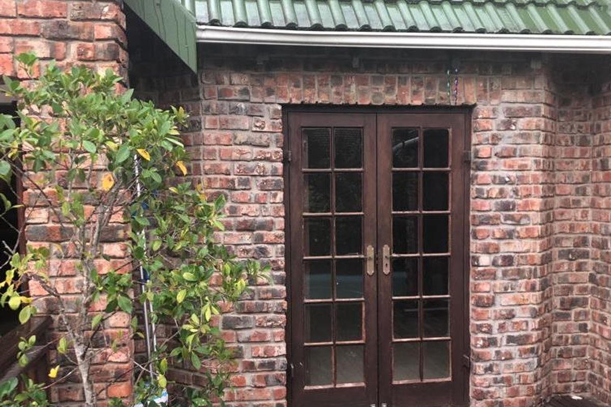 Rear exterior view featuring exposed brickwork, double french doors, and a timber deck under a tiled roof.