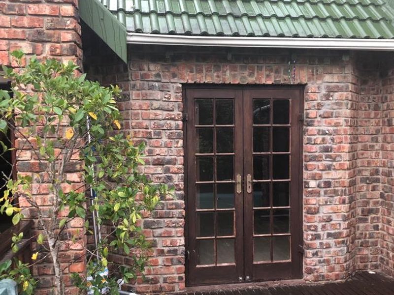 Rear exterior view featuring exposed brickwork, double french doors, and a timber deck under a tiled roof.
