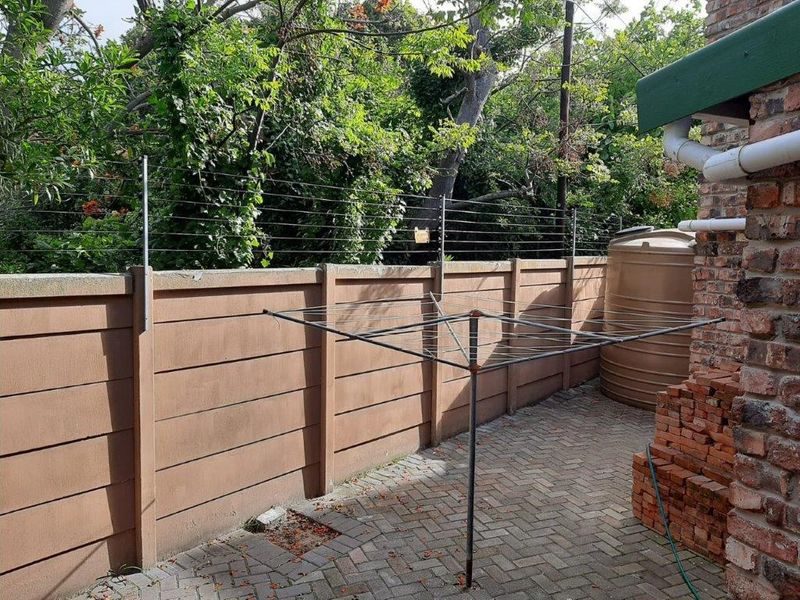 Rear exterior area featuring a precast concrete boundary wall with electric fencing, paved patio surface, and a water storage tank.