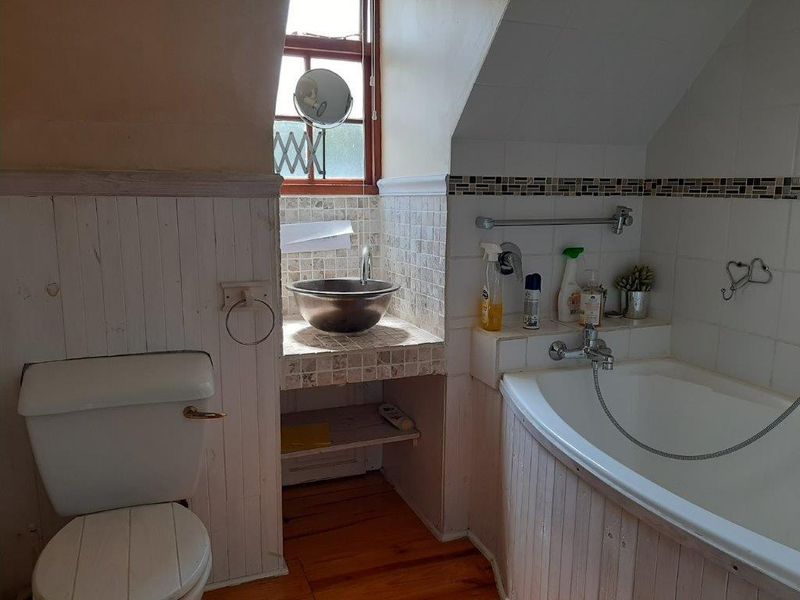 Compact bathroom featuring a vessel sink on a tiled vanity, bathtub with handheld shower mixer, and timber wall paneling under a sloped ceiling.