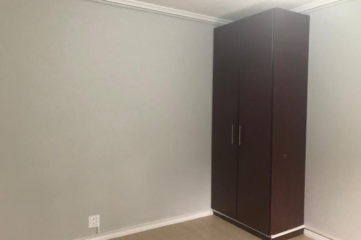 A clean, empty bedroom featuring neutral wall paint, tiled flooring, and a dark wood built-in cupboard.