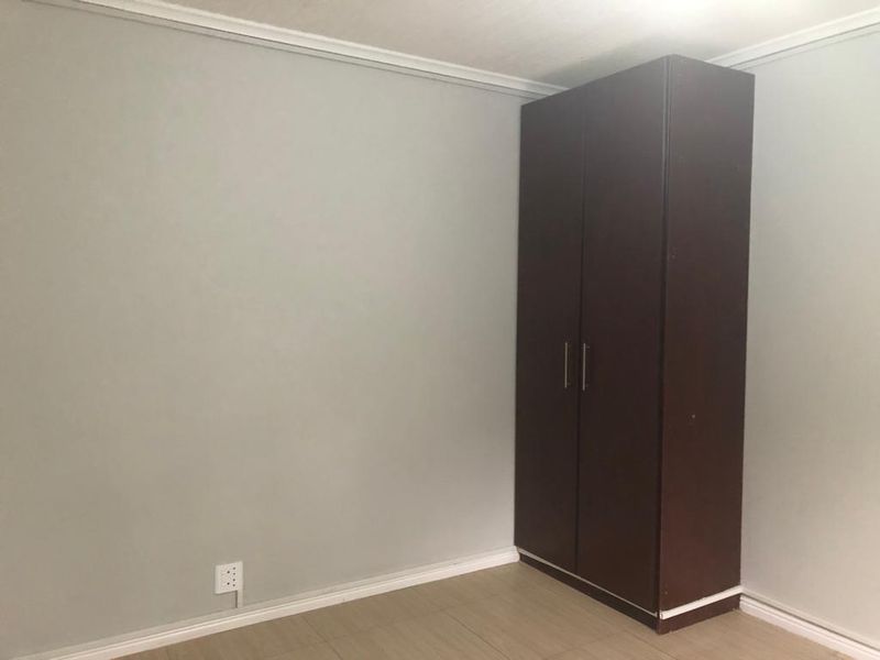 A clean, empty bedroom featuring neutral wall paint, tiled flooring, and a dark wood built-in cupboard.